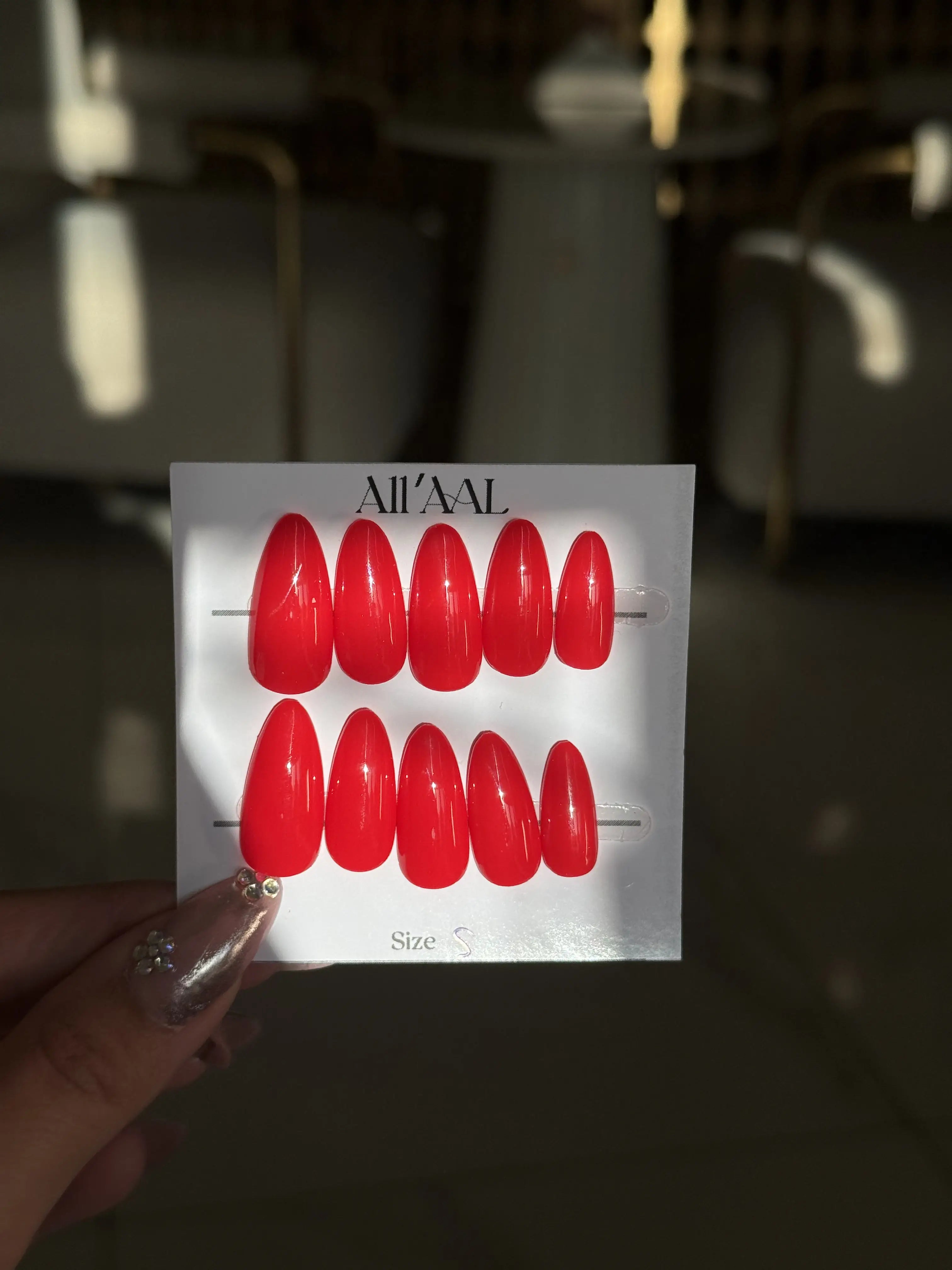 Red nail art display with 'AII'AAL' branding held by a hand.