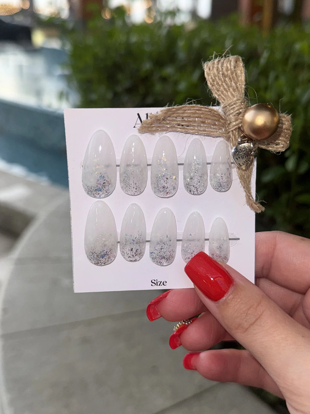 Nail art stickers on a card held by a person with red nails outdoors.