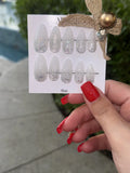 Card with glittery nail designs held by a hand with red nails outdoors.