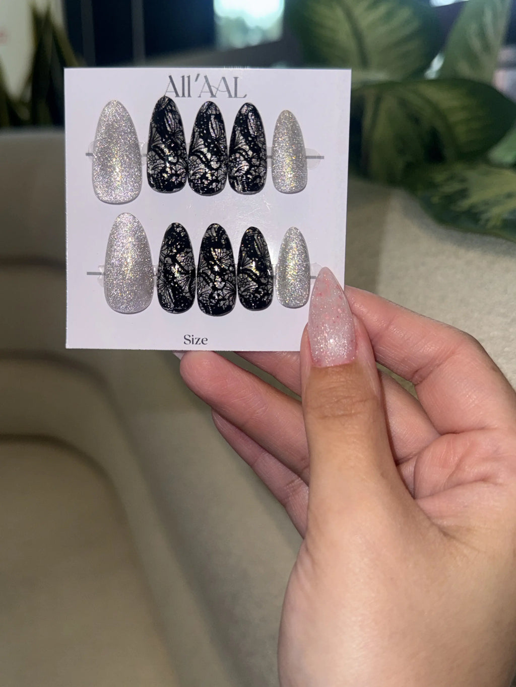 Hand holding a card with nail art designs and a person's nail with similar design.