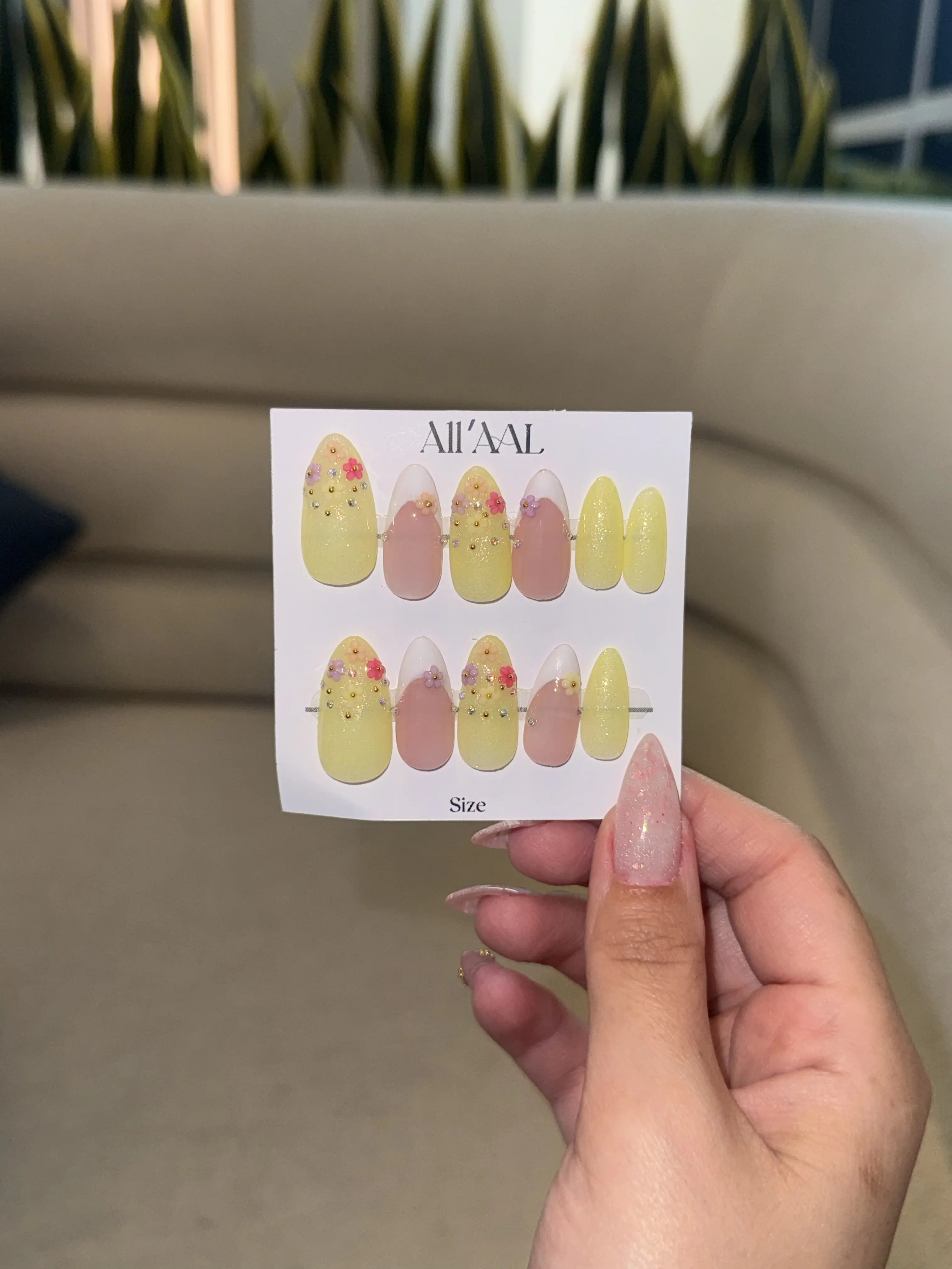 Hand holding a card with nail art designs by All'Al against a neutral background