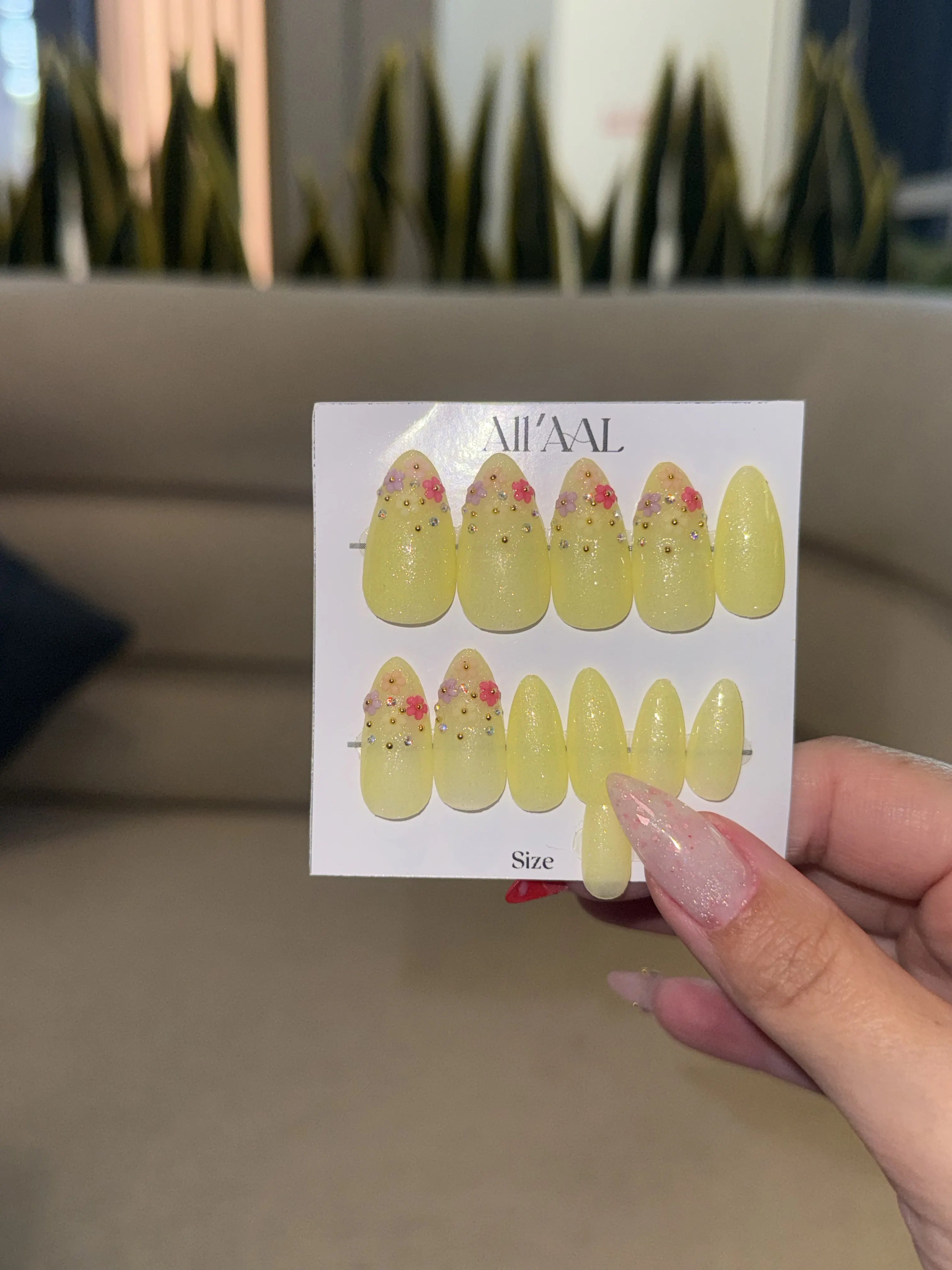 Card with yellow nail art designs held by a hand against a blurred indoor background