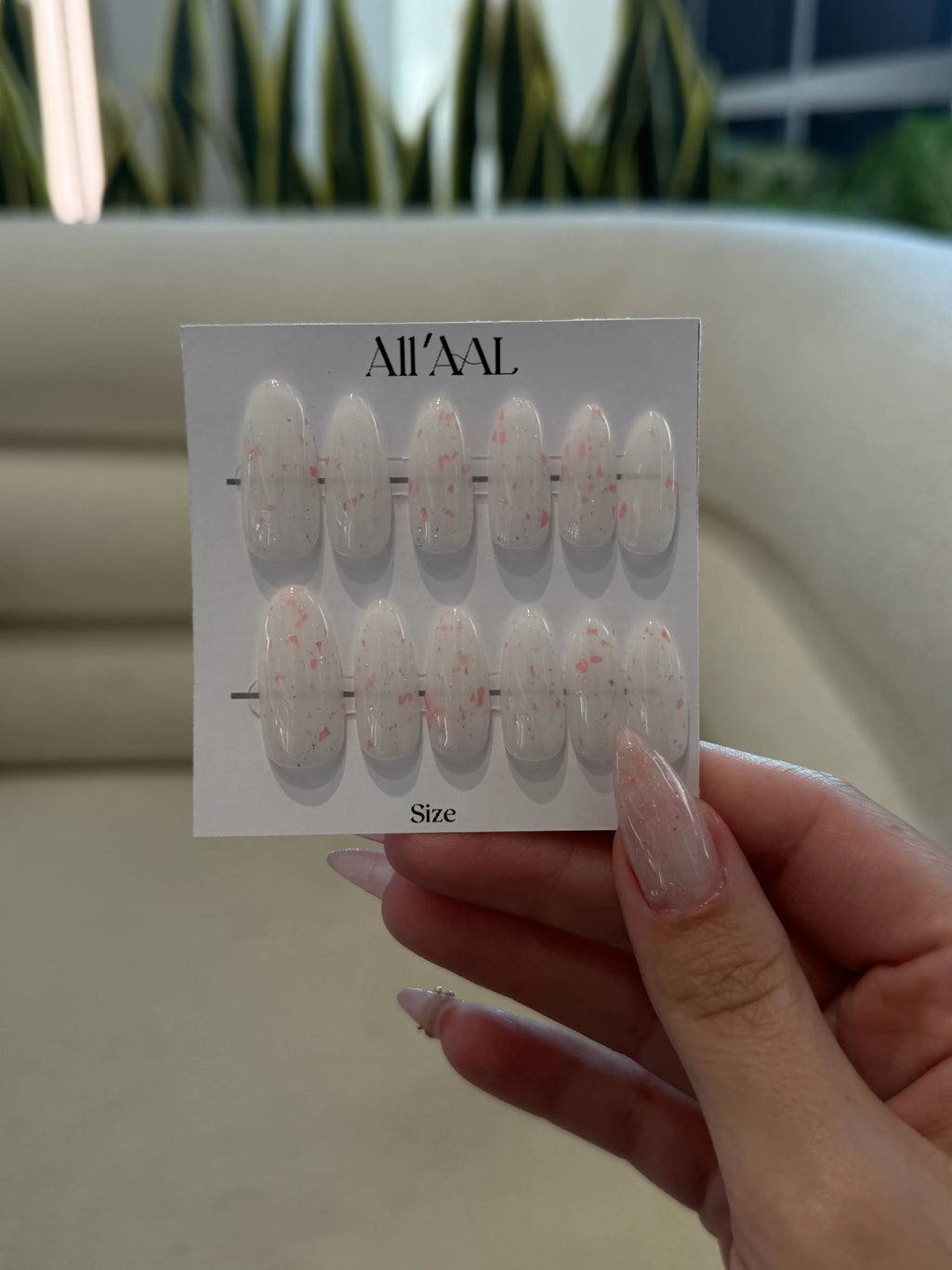 Hand holding a card with nail art designs labeled 'All'AAAL' against a blurred outdoor background.