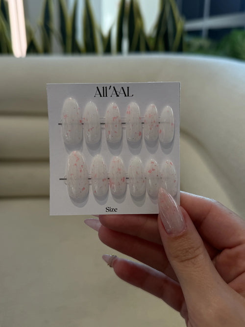 Hand holding a card with nail art designs labeled 'All'AAAL' against a blurred outdoor background.