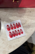Red nail art display sheet on a marble surface with a red handbag in the background.