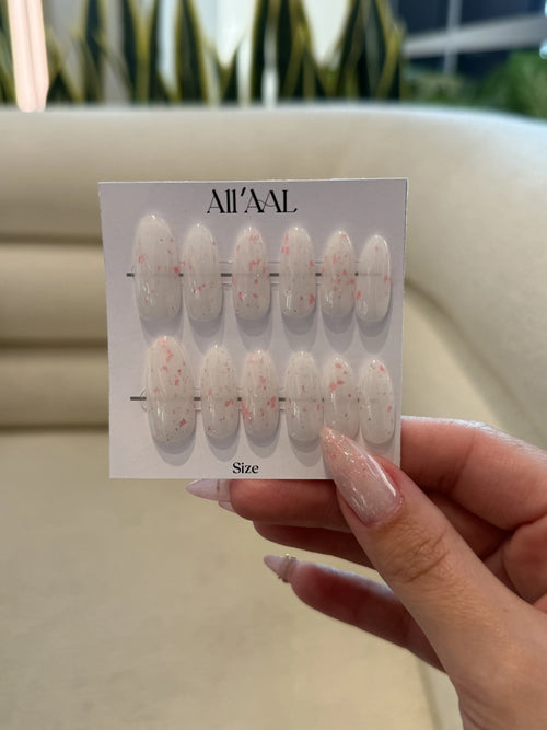 Hand holding a card with nail art designs labeled 'All'Al' against a blurred indoor background.