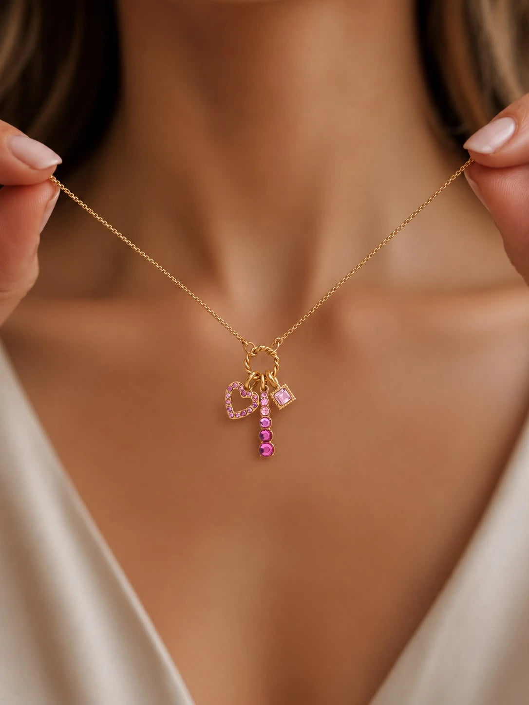 A close-up of a model wearing a delicate gold necklace with a charm shaped like a pink bow and a small pink heart pendant.